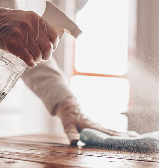 A person cleaning a wooden table with a spray bottle.